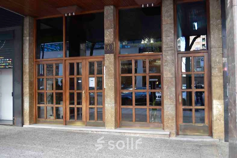 Exterior view of the office building at Calle Capitan Haya 60, Madrid Tetuán, showcasing large wooden doors and street reflections, ideal for office space rental.
