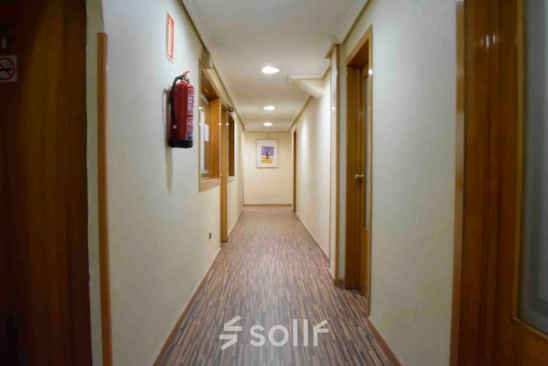 A long, well-lit corridor with wooden doors, located in an office to rent at Calle Capitan Haya 60, Madrid Tetuán.