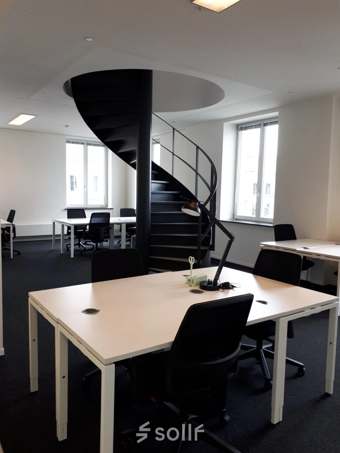 Modern office space with spiral staircase at Kardinaal Mercierplein 2 in Mechelen Centrum, available for rent. Features multiple desks and chairs, creating an inviting workspace atmosphere.