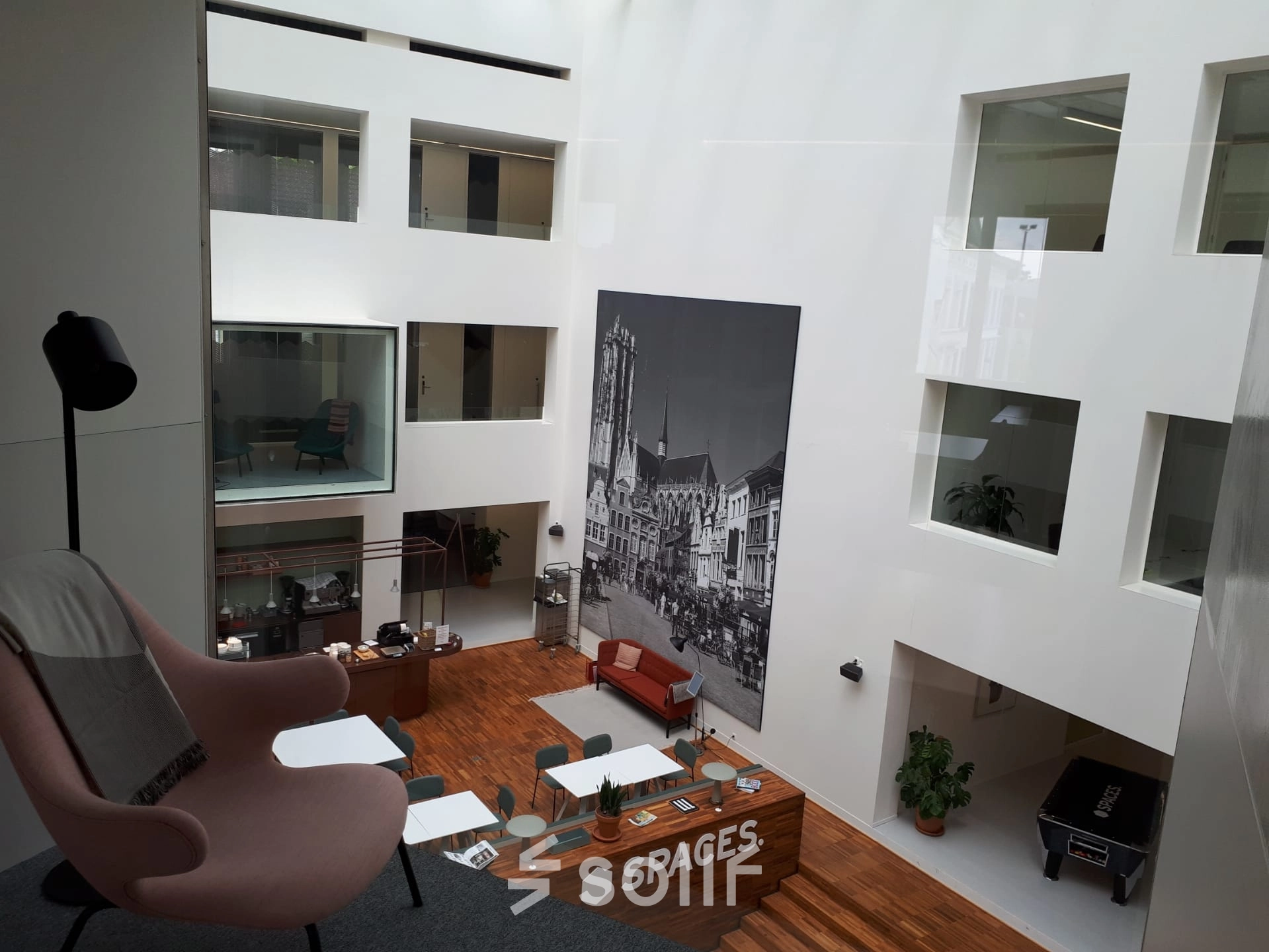 A modern office space rental in Mechelen Centrum featuring a bright, open atrium with a seating area and large artwork on the wall. Ideal office to rent for meetings or collaboration.