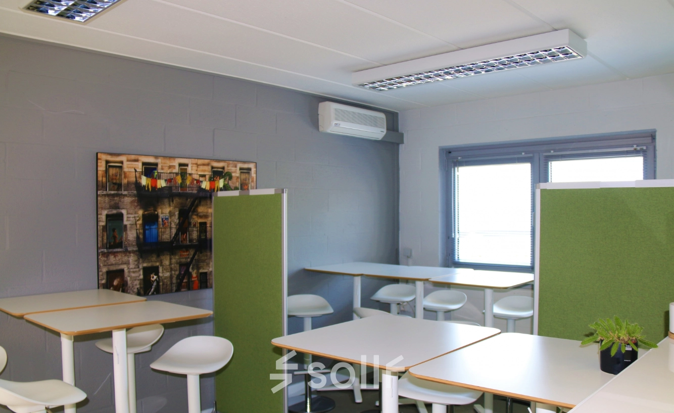 Furnished office space rental at De Regenboog 11 in Mechelen North with white tables, green dividers, and tall chairs under bright lighting.