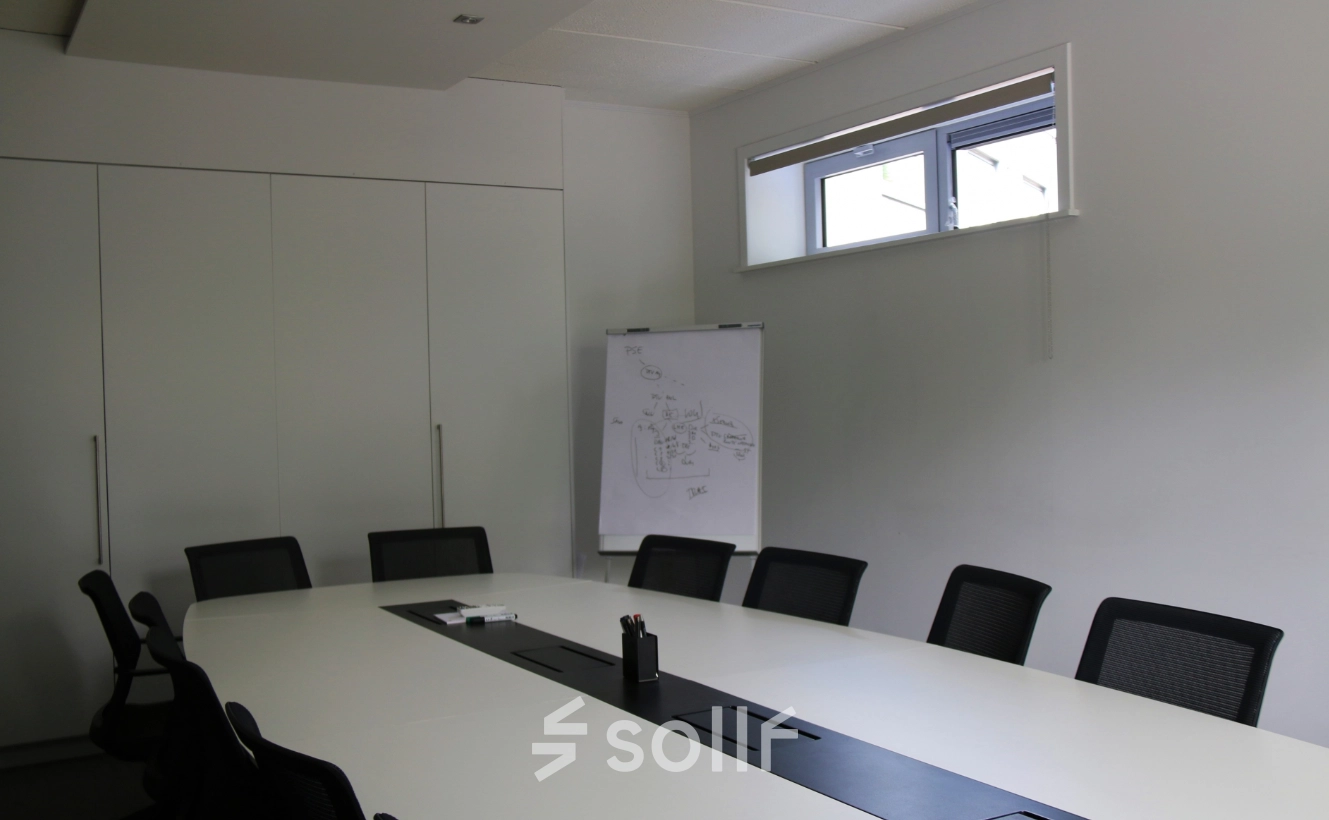 Conference room with a long white table, black chairs, and a flip chart in an office for rent at De Regenboog 11, Mechelen North.