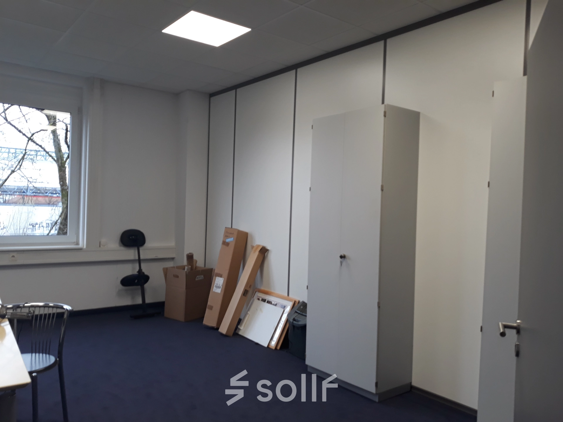 Unfurnished office space for rent on Landsberger Straße, featuring a window, chairs, cabinets, and boxes against carpeted flooring. Ideal for workspaces in München Pasing.