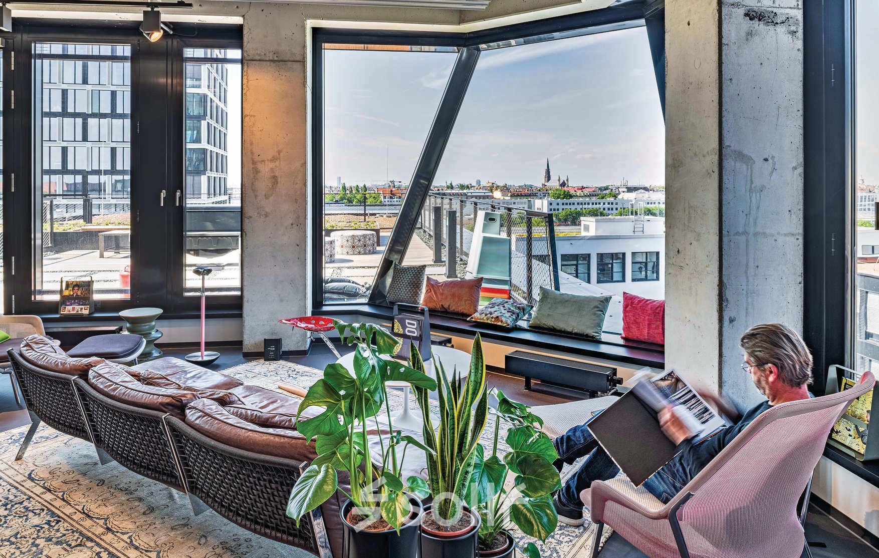 Bright, furnished office space at Rosenheimer Straße 143C, München Werksviertel, featuring large windows with a city view and a person reading.