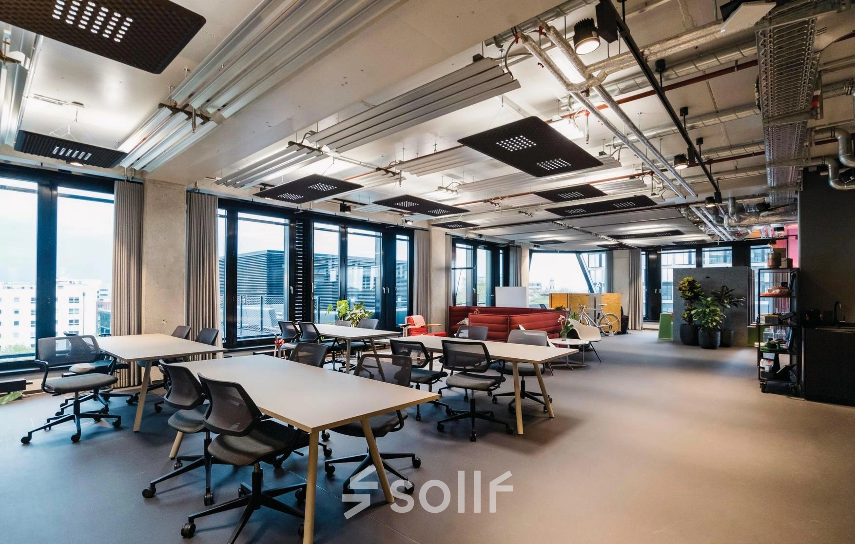 Spacious office to rent at Rosenheimer Straße 143C, featuring modern furnishings and several desks under industrial ceilings, perfect for collaborative work. Bright windows enhance the inviting workspace.