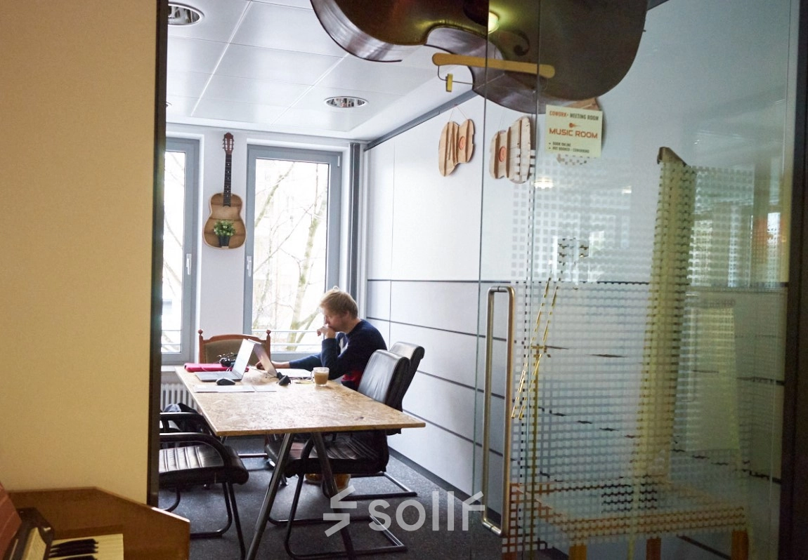 Cozy office space with a person working at a desk, decorated with wall-mounted guitars. Ideal for office space rental in Munich Giesing.