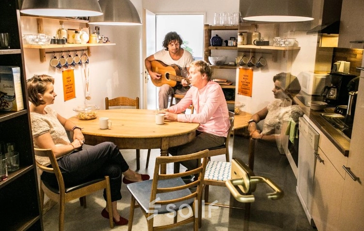 Cozy furnished office space at Werinherstraße 3, Munich Giesing, featuring a kitchen area with employees enjoying coffee and a colleague playing the guitar. Ideal for office space rental.