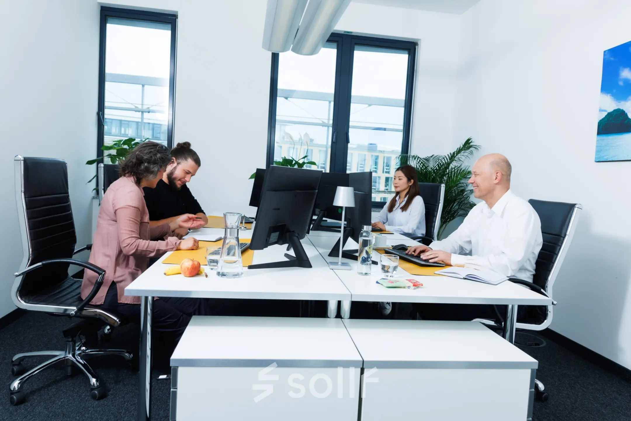 People collaborating in a modern, furnished Munich Laim office space with computers and documents on white desks, available for office space rental.
