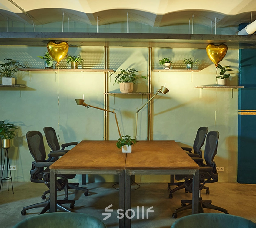 Furnished interior of a cozy office for rent at Amalienstraße 71, Munich Maxvorstadt, featuring wooden tables, chairs, decorative plants, and warm lighting, ideal for workspace and office space rental.
