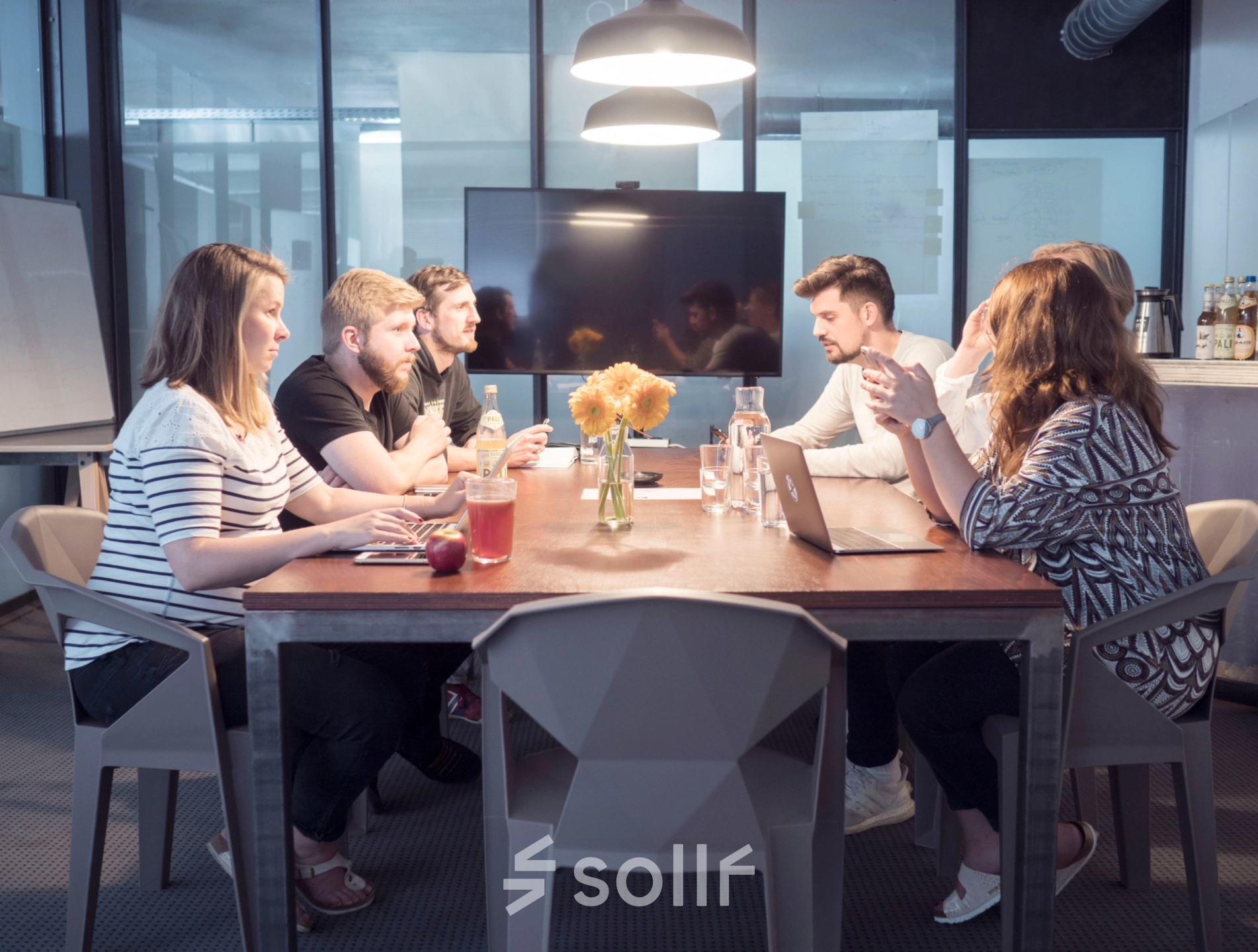 People collaborating in a furnished office space with a large table and modern decor. Ideal for rent office space in Munich Maxvorstadt.