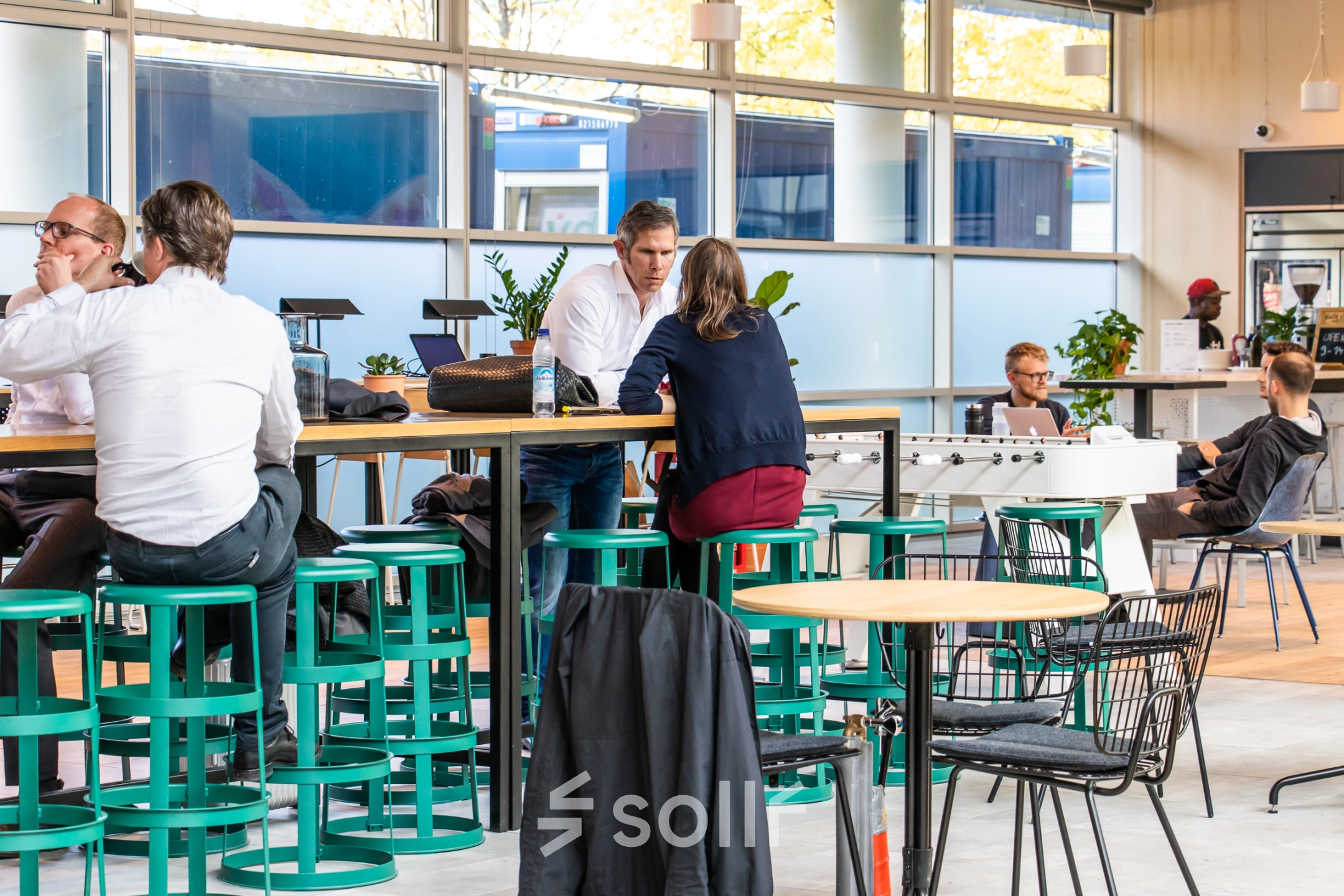 Modern office space available for rent in Munich Maxvorstadt at Oskar-von-Miller-Ring 20, featuring professionals engaged in discussions and working at tables surrounded by greenery and natural light.