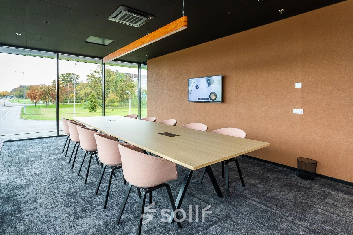 Modern conference room with a long wooden table and pink chairs at Jonkerbosplein 52 in Nijmegen, ideal for office space rental.