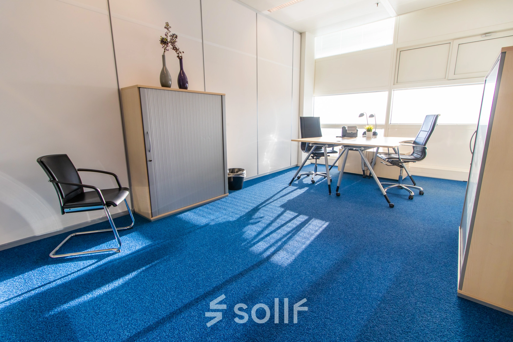 Bright office space with blue carpet, modern furniture, and natural light at Jonkerbosplein 52, Nijmegen, perfect for office space rental.