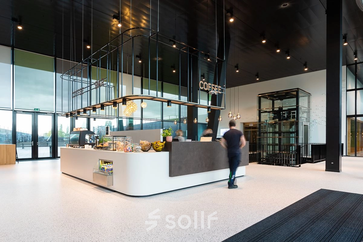 Modern office interior at Jonkerbosplein 52 in Nijmegen featuring a stylish coffee bar with people engaged in business activities, ideal for office space rental.