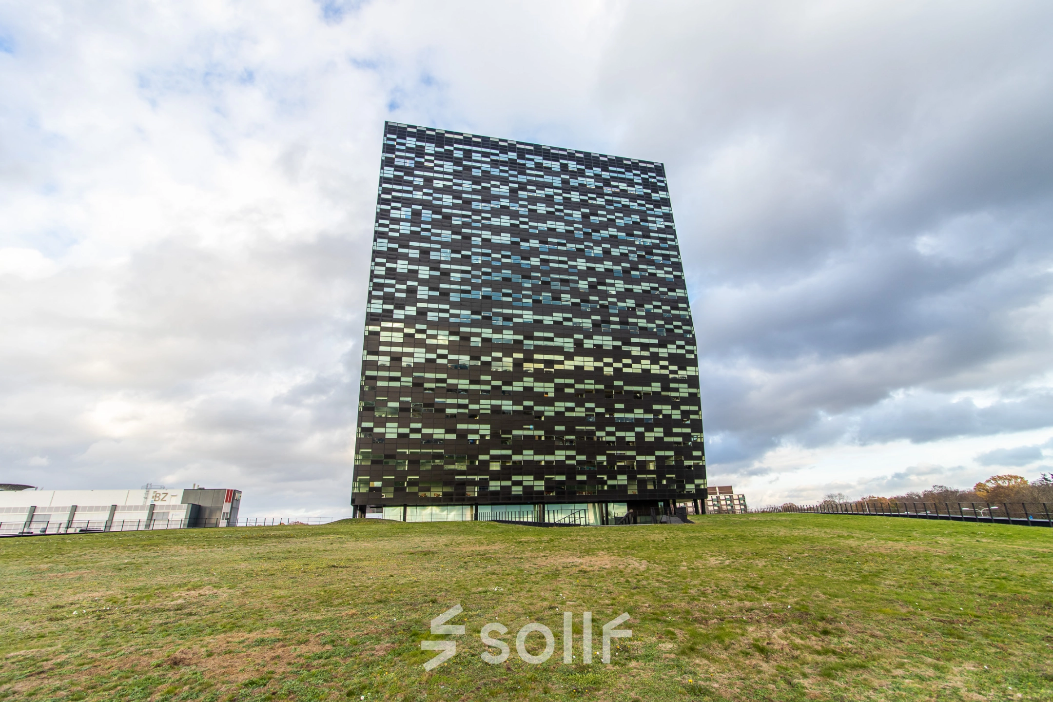 Exterior view of the modern office building for rent at Jonkerbosplein 52, Nijmegen, featuring a checkerboard facade and surrounding green space.