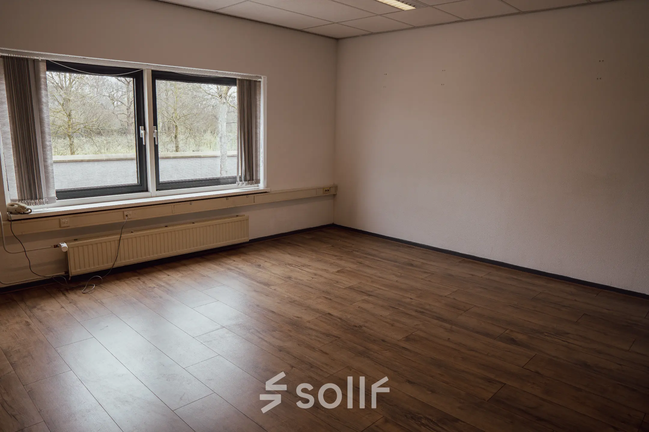 An empty interior space with wooden flooring and a large window, ideal for those seeking office space rental in Oosterhout Nb.