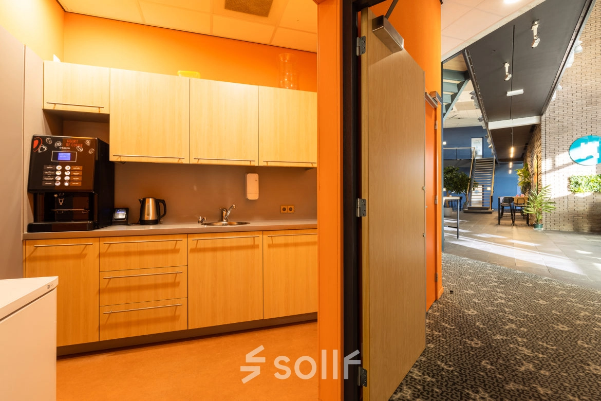 Interior view of a furnished office space with a pantry area, featuring wooden cabinets, a coffee machine, and a kettle. Ideal office space rental opportunity at Veengang 1, Oosterwolde.