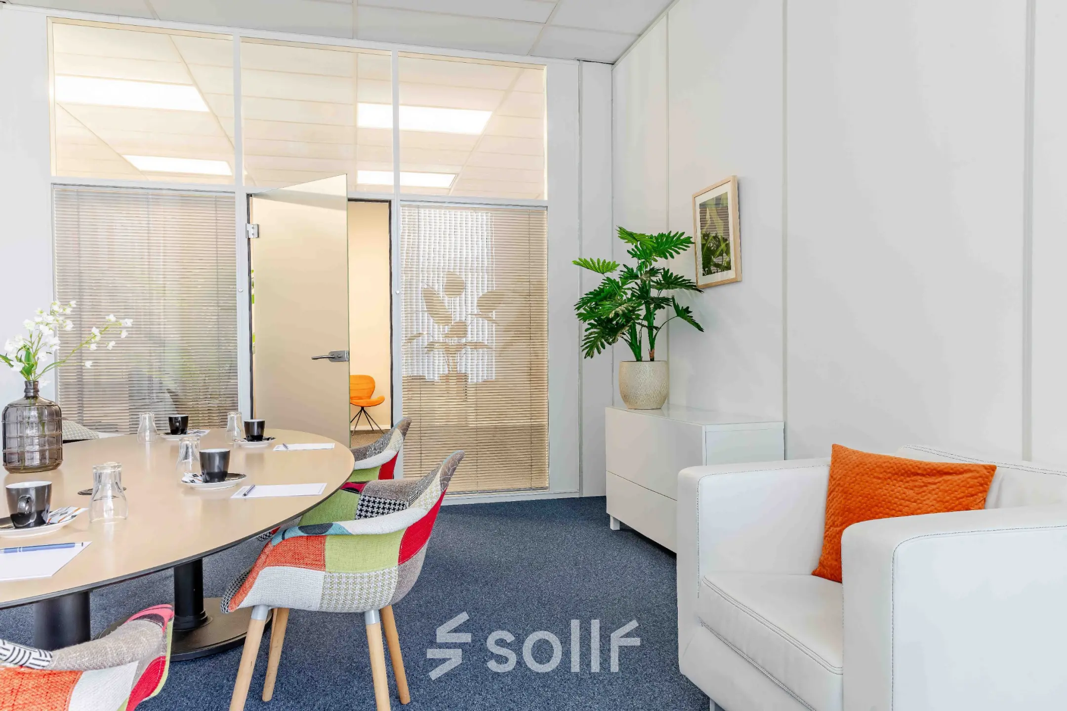 Bright office space with a round meeting table, colorful chairs, and a cozy seating area, ideal for office space rental in Reeuwijk.