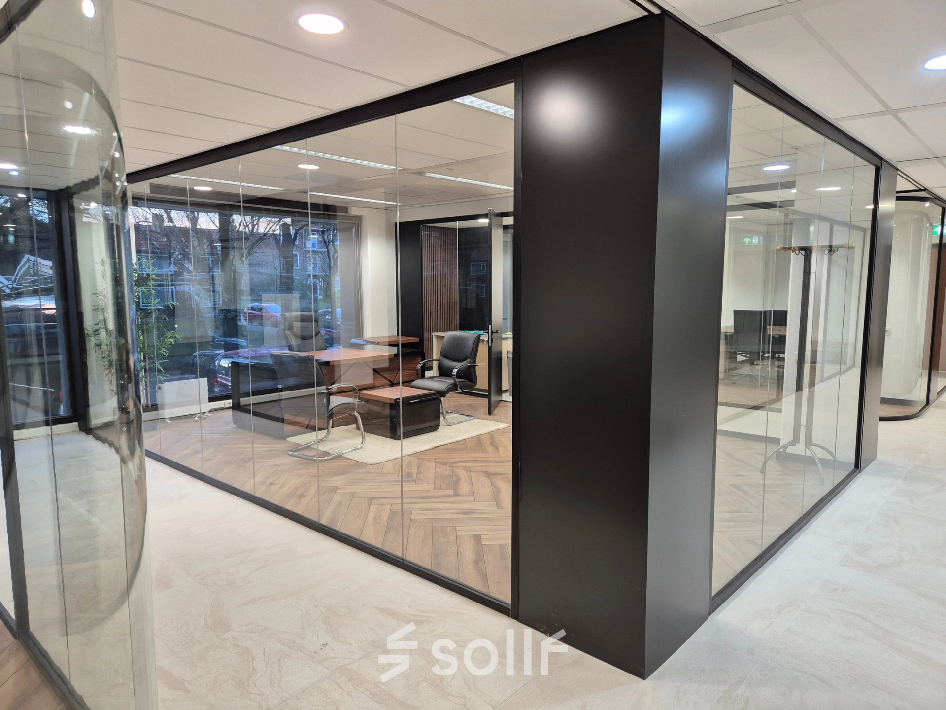 Modern office space rental located at JC van Markenlaan 3, Rijswijk, featuring glass walls, stylish wooden flooring, and contemporary seating arrangements.