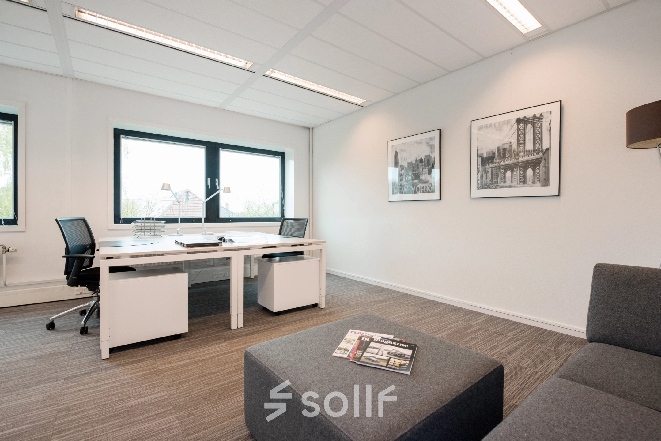 Bright office space with modern furnishings, featuring a large window and artwork on the walls. Ideal for office space rental.
