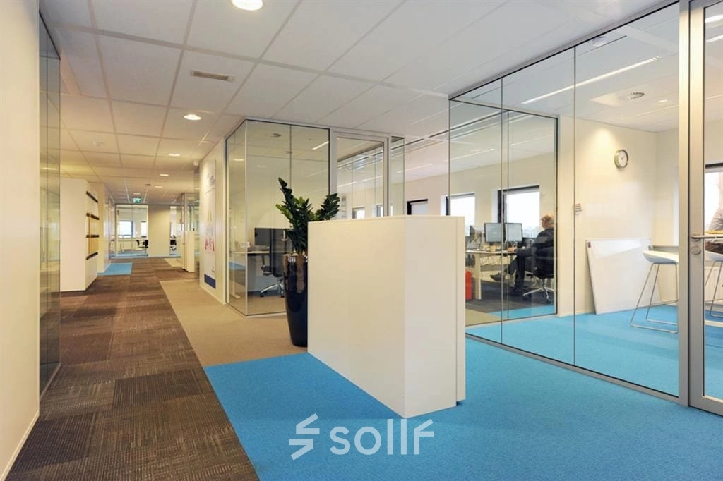 Modern office to rent at Patrijsweg 62, Rijswijk, featuring glass-walled workspaces and a blue carpet. Ideal for office space rental.
