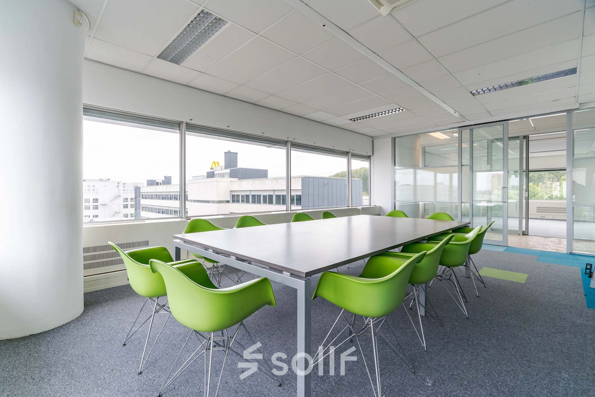 Bright office space for rent at Polakweg 7, Rijswijk, featuring a large meeting table surrounded by green chairs, ideal for collaborative work.