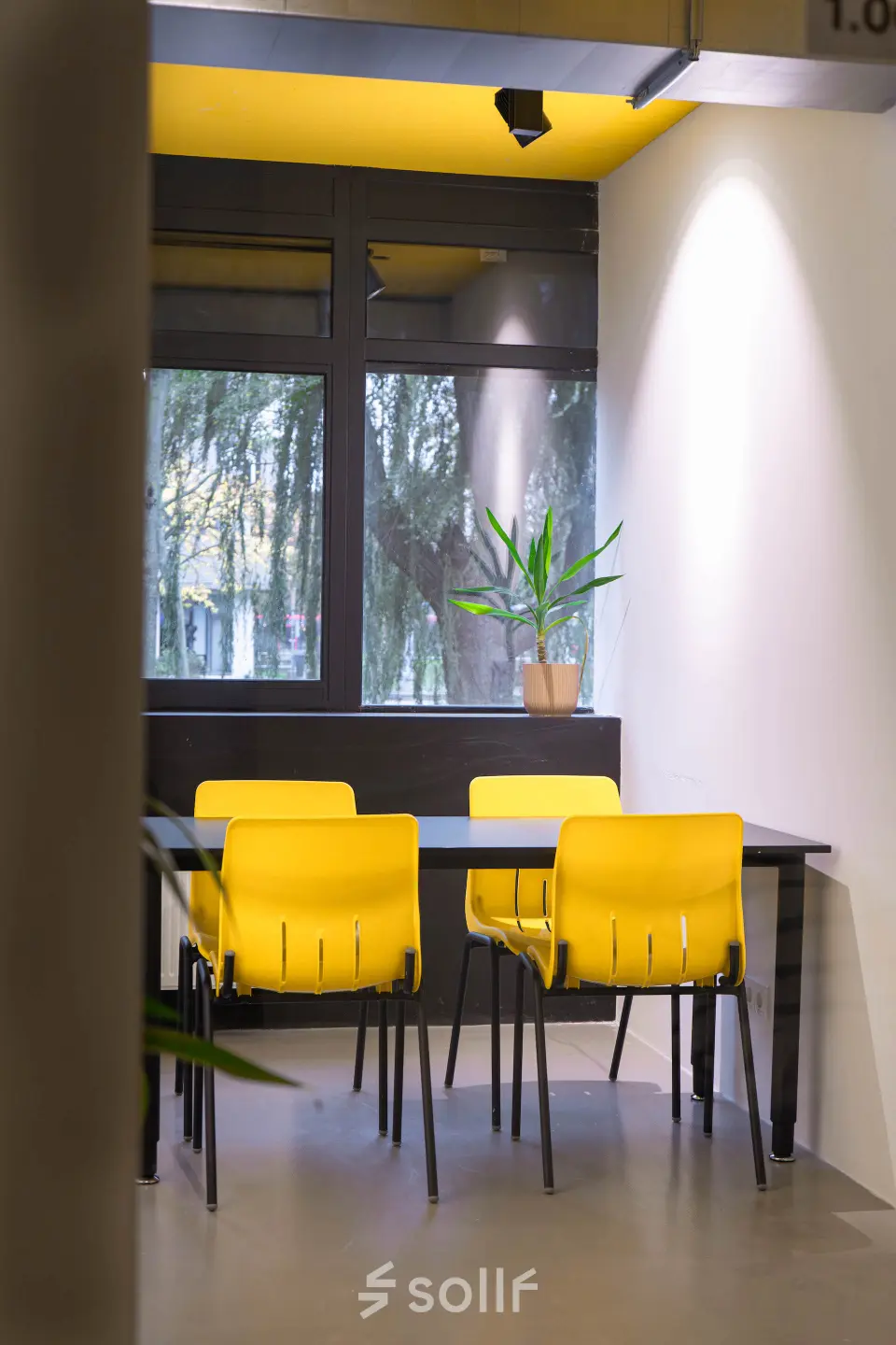 Office space for rent at Volmerlaan 7, Rijswijk, featuring bright yellow chairs around a table with a potted plant against a window backdrop.