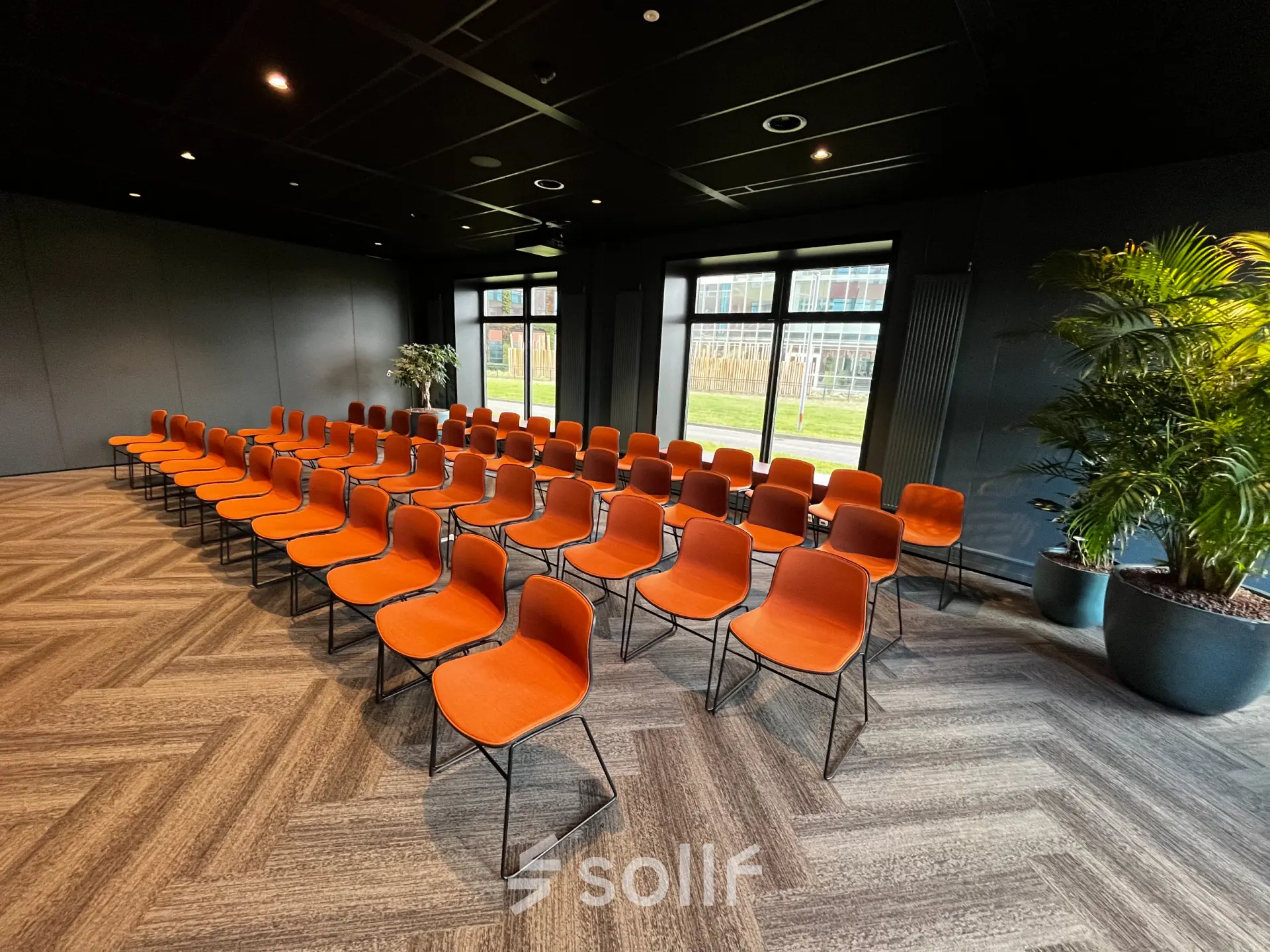 Spacious office space to rent in Rotterdam Alexander featuring rows of orange chairs facing windows with green views, perfect for meetings or presentations.
