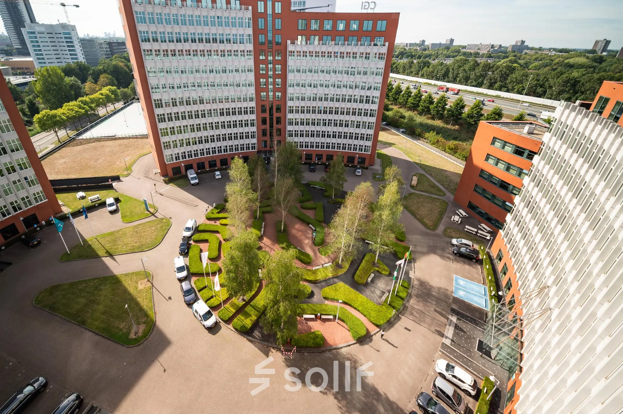 View of the office complex at George Hintzenweg 77 - 89 in Rotterdam Alexander, featuring multiple tall buildings surrounding a landscaped courtyard with neatly trimmed greenery and parked cars. Ideal office space rental location.