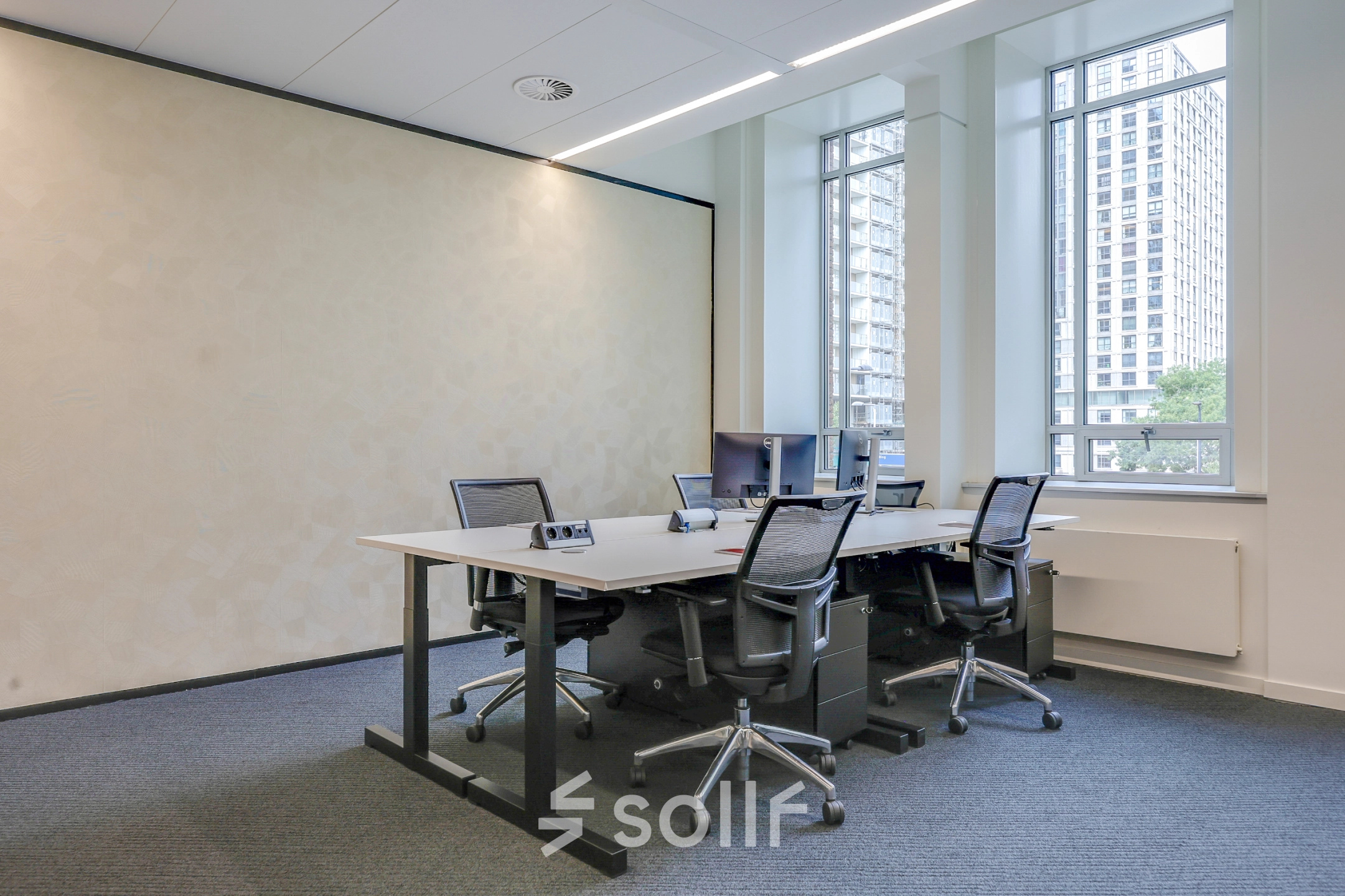 Modern office space rental at Blaak 34, Rotterdam Center, featuring a bright workspace with several desks and chairs by large windows.