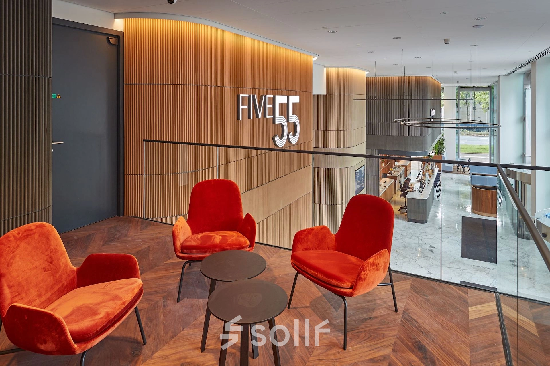 Modern office lounge area at Blaak 555, Rotterdam Center, featuring stylish red chairs and wood paneling. Ideal office space rental opportunity.