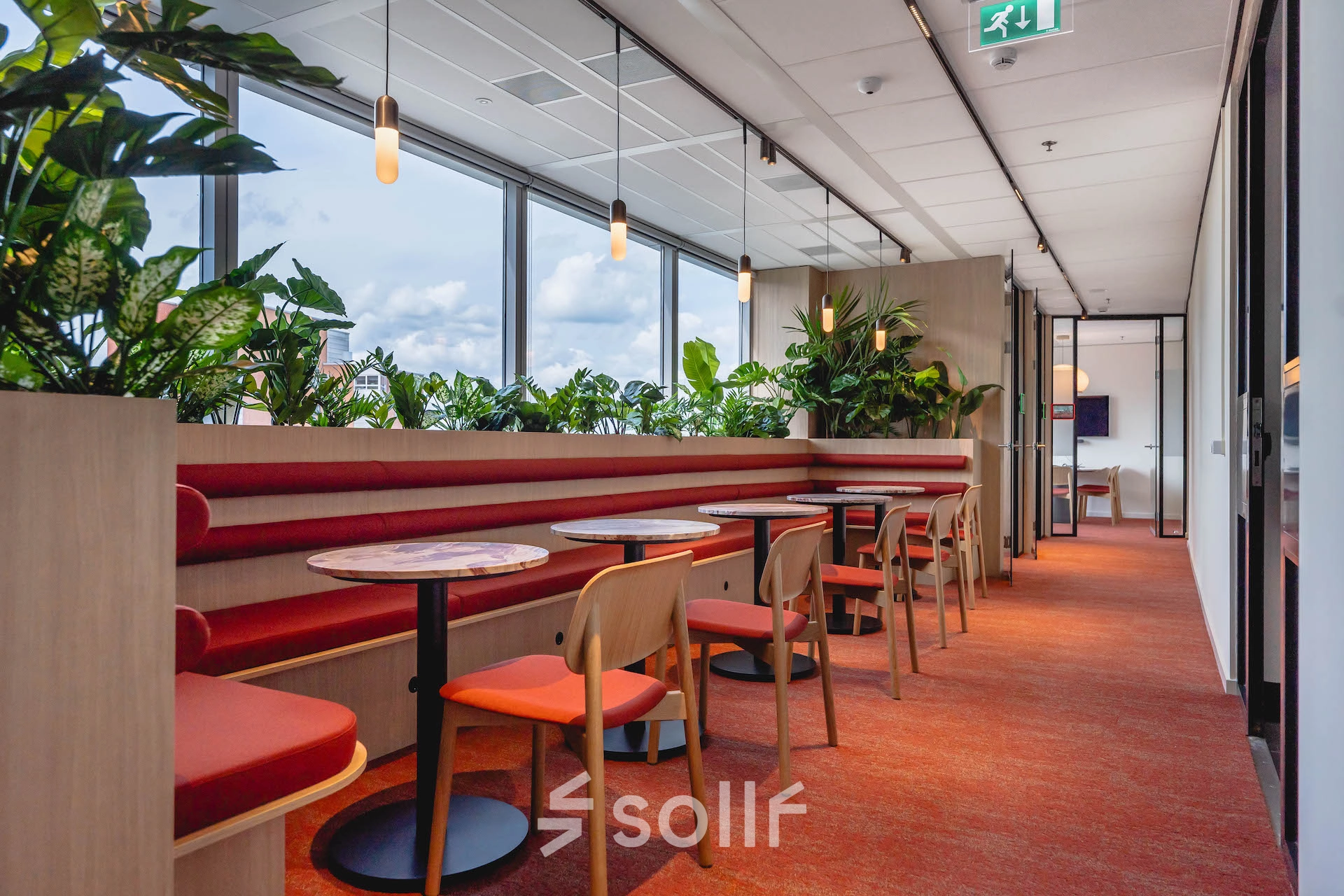 Bright workspaces at Blaak 555 in Rotterdam Center, featuring vibrant red seating and lush plants, available for office space rental.