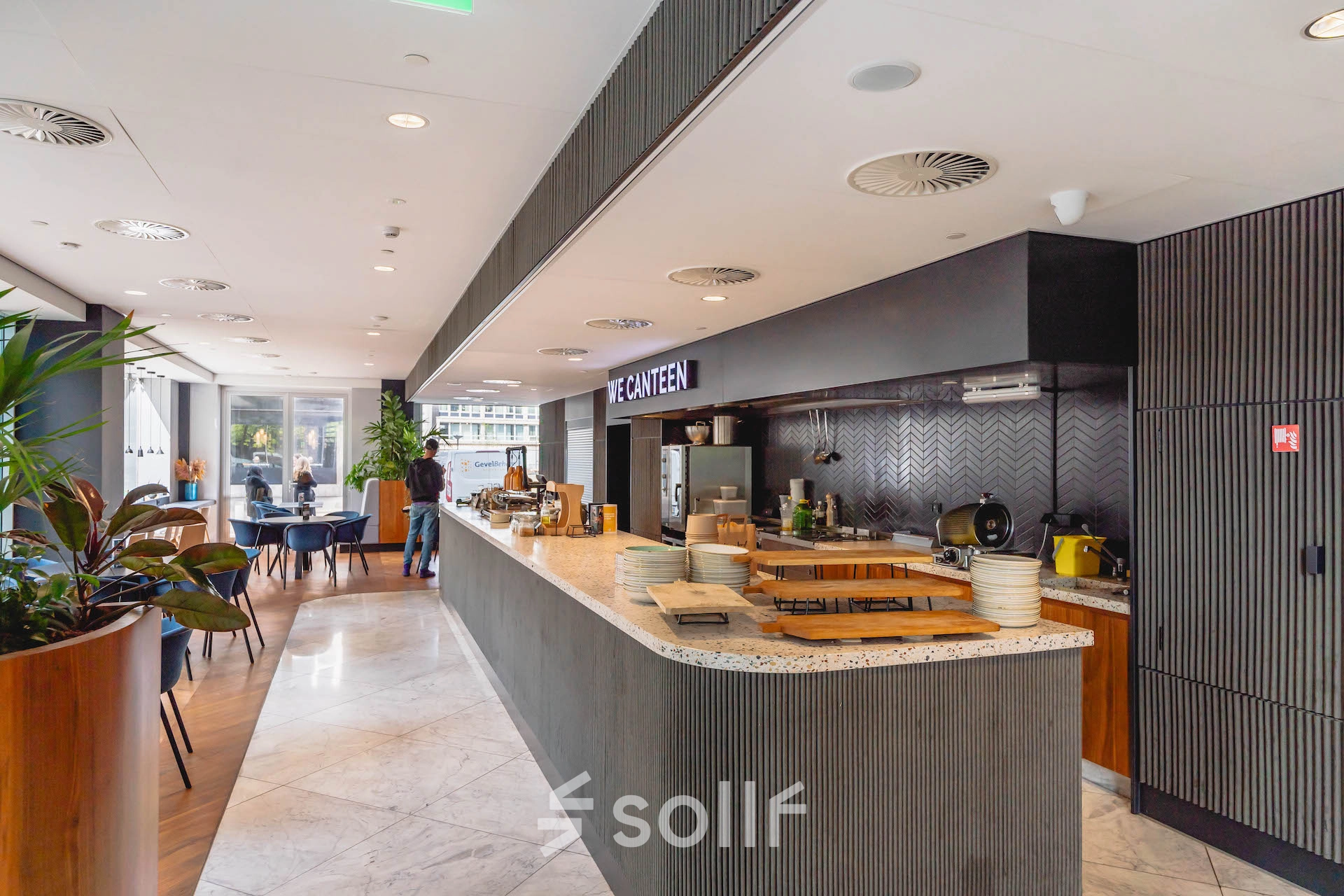 Interior of Blaak 555, Rotterdam Center, featuring a modern canteen area. A person is preparing food at the counter, suitable for office space rental.