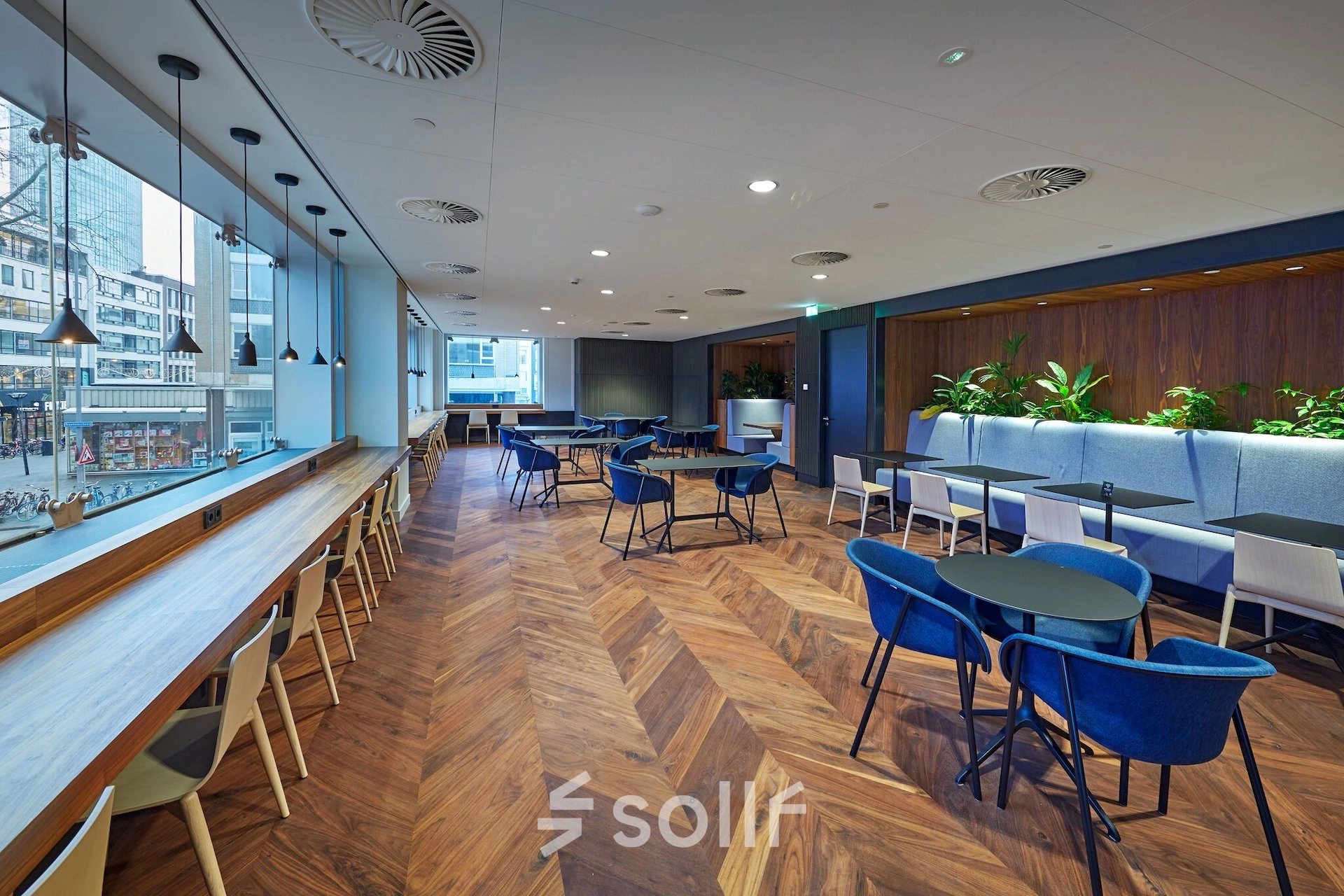 Spacious office in Blaak 555, Rotterdam Center, featuring modern workspaces with blue seating, wood flooring, and large windows ideal for office space rental.