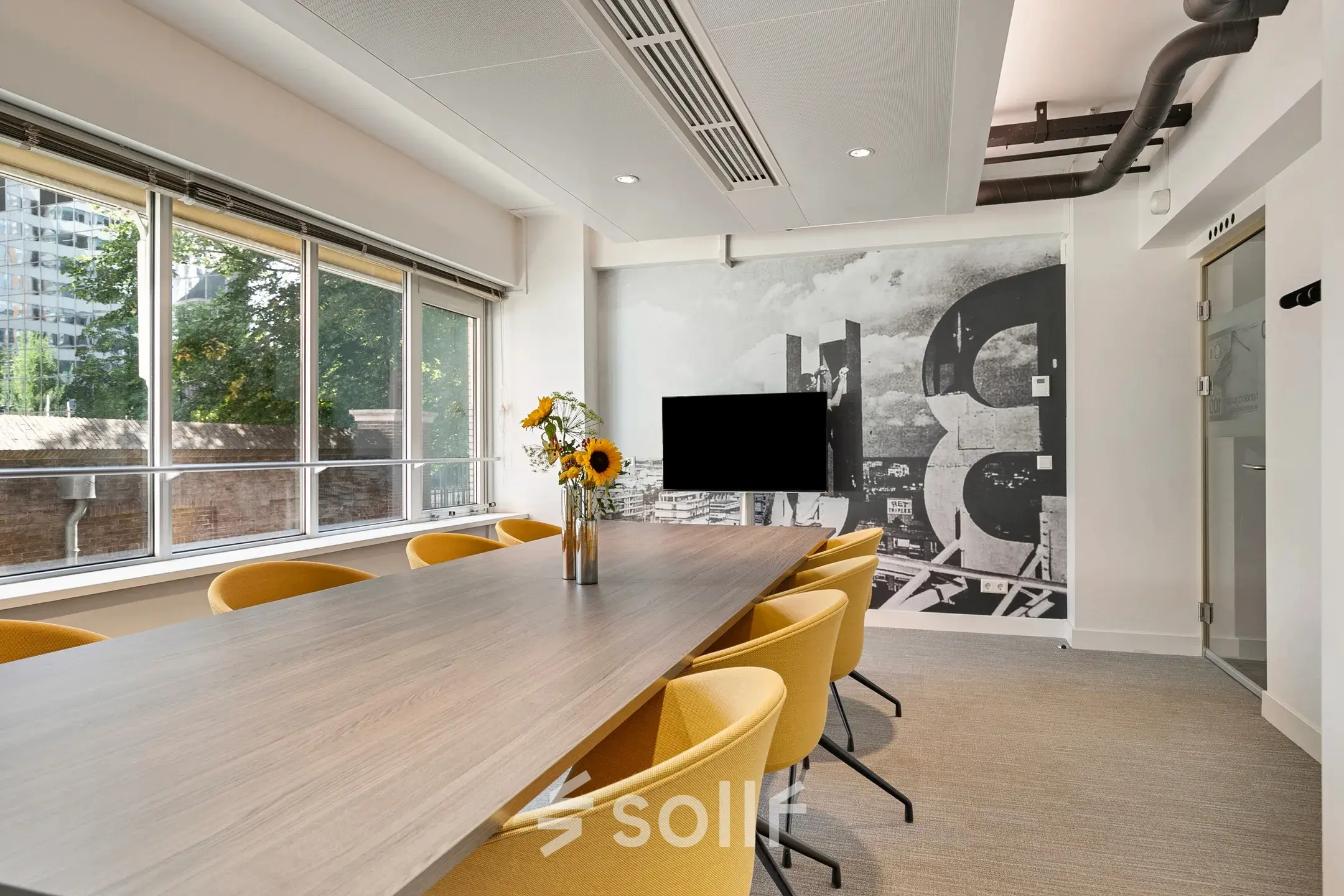 Bright conference room with a long table and yellow chairs, featuring large windows and a modern wall design. Ideal office space rental in Rotterdam Center at Coolsingel 104.