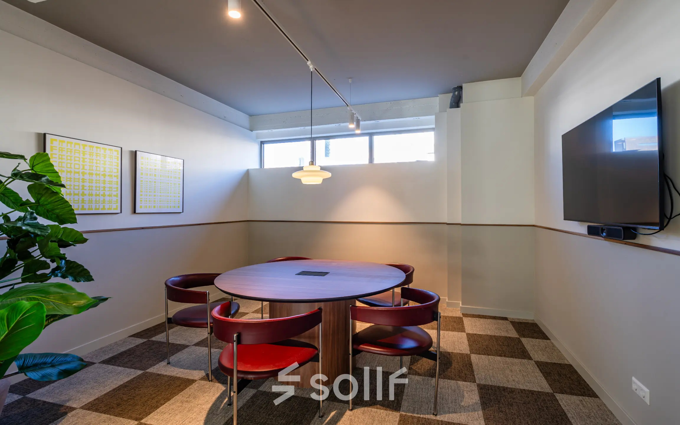Cozy conference room with a round table, red chairs, wall art, and a large screen at Stadhuisplein 9-23 in Rotterdam Center, ideal for office space rental.