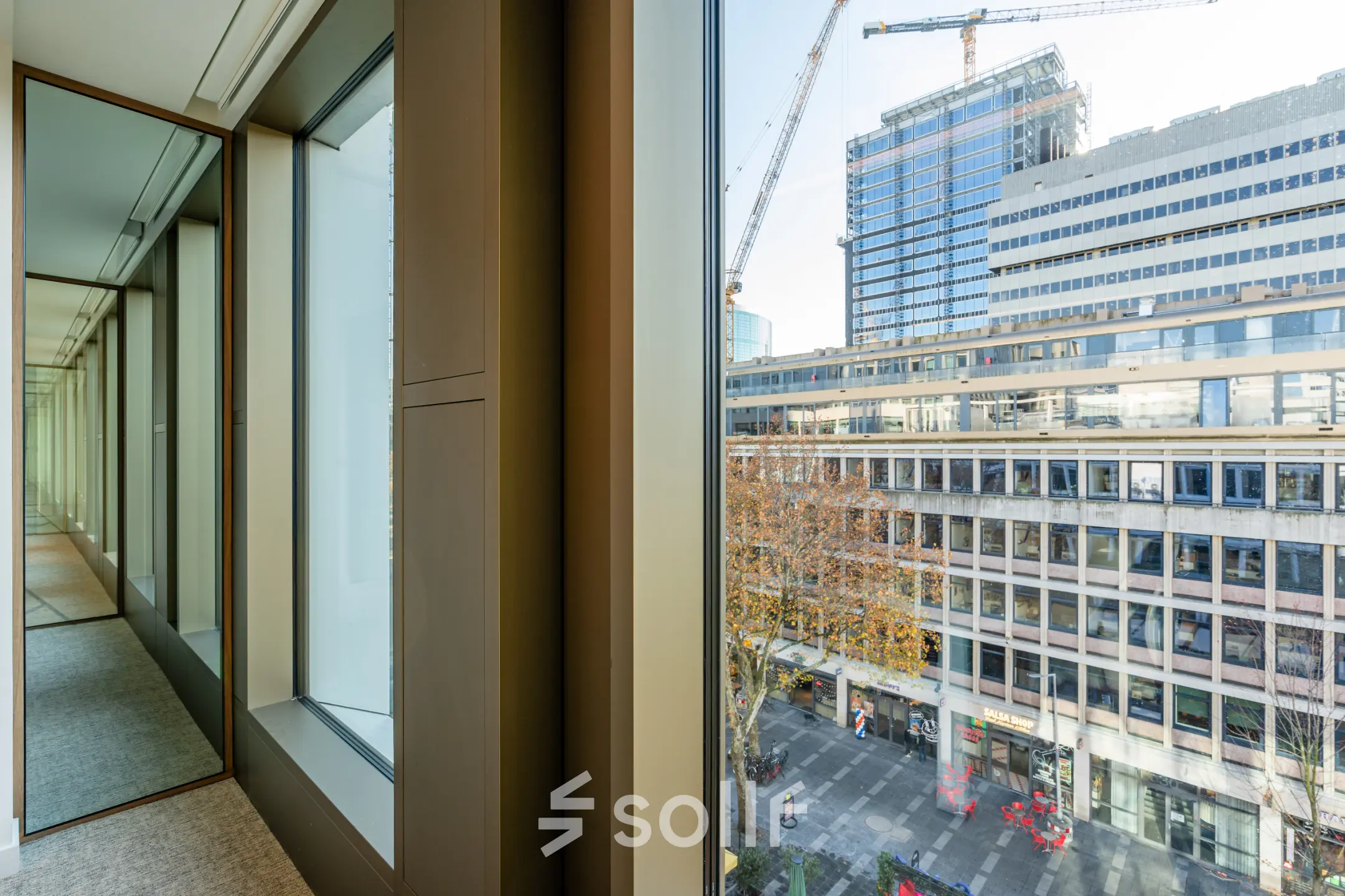 View from the interior of an office space in Stadhuisplein 9-23, Rotterdam Center, overlooking urban buildings and a construction site, ideal for office space rental.