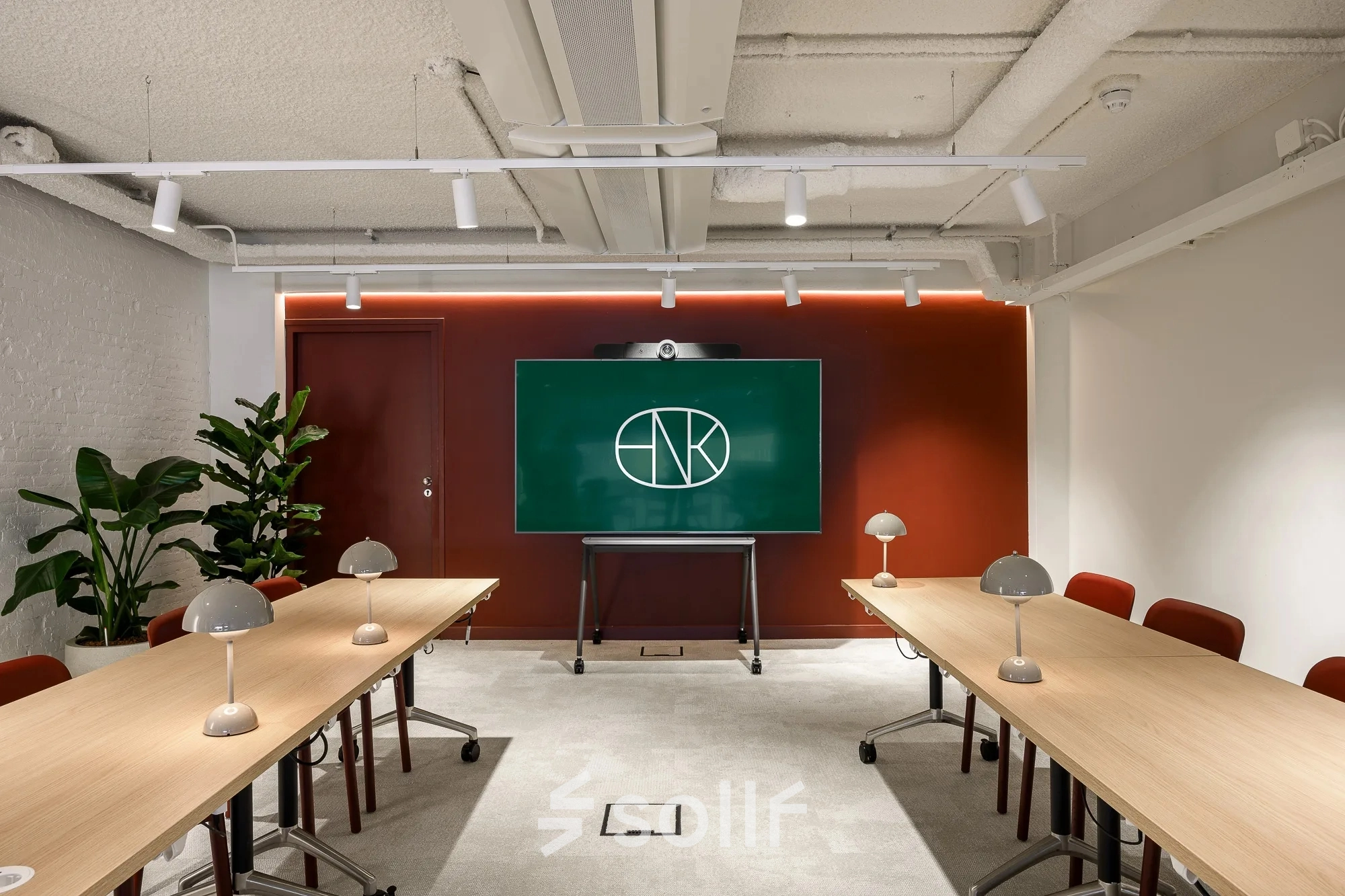 Modern conference room in office space rental at Vasteland 42-110, Rotterdam Center, featuring two long tables, chairs, lamps, and a digital screen.