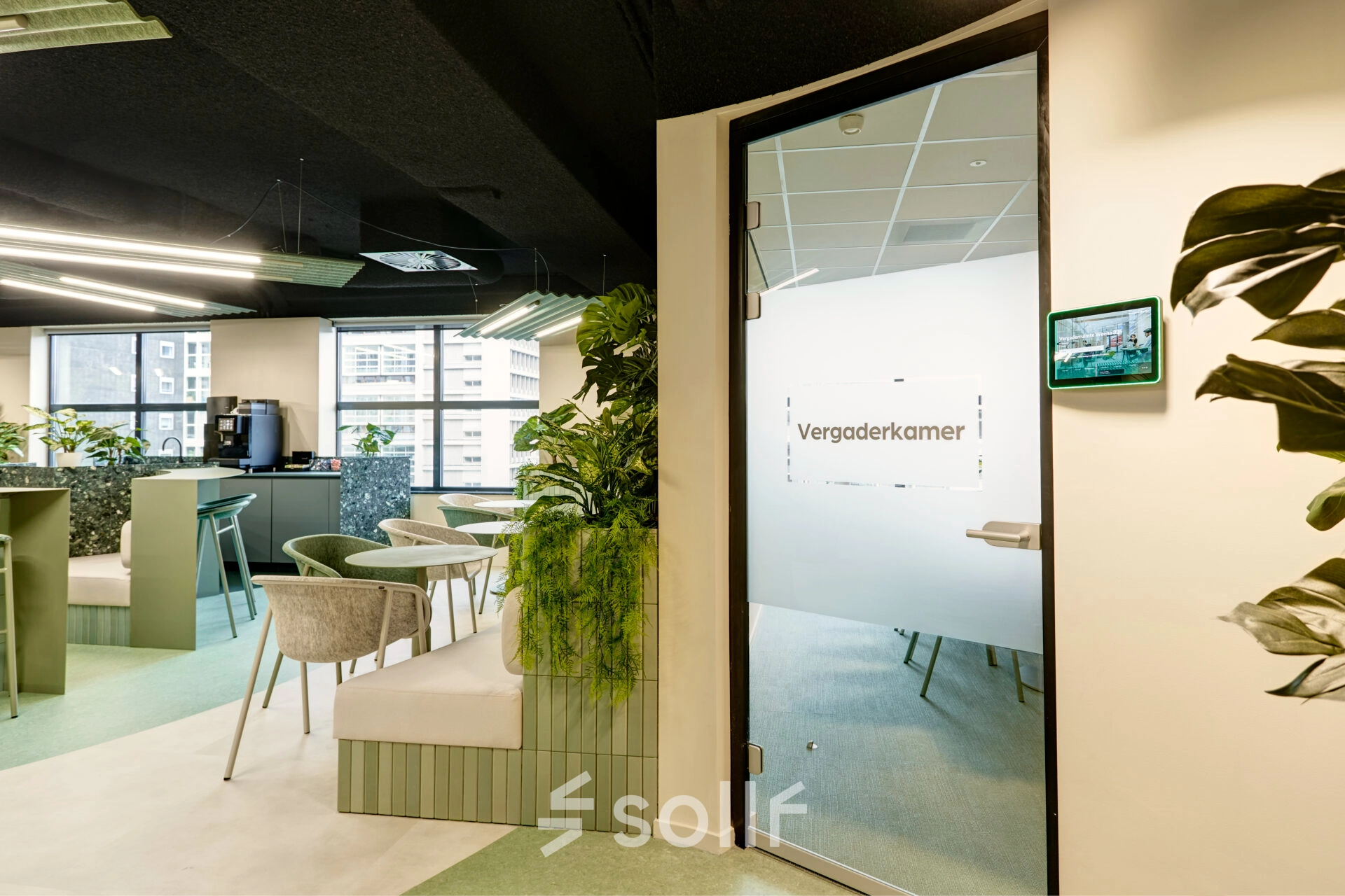 Modern office space rental at Weena 335, Rotterdam Center, featuring stylish furniture and a meeting room labeled 'Vergaderkamer'. Decorative plants add a refreshing touch to the open workspace environment.