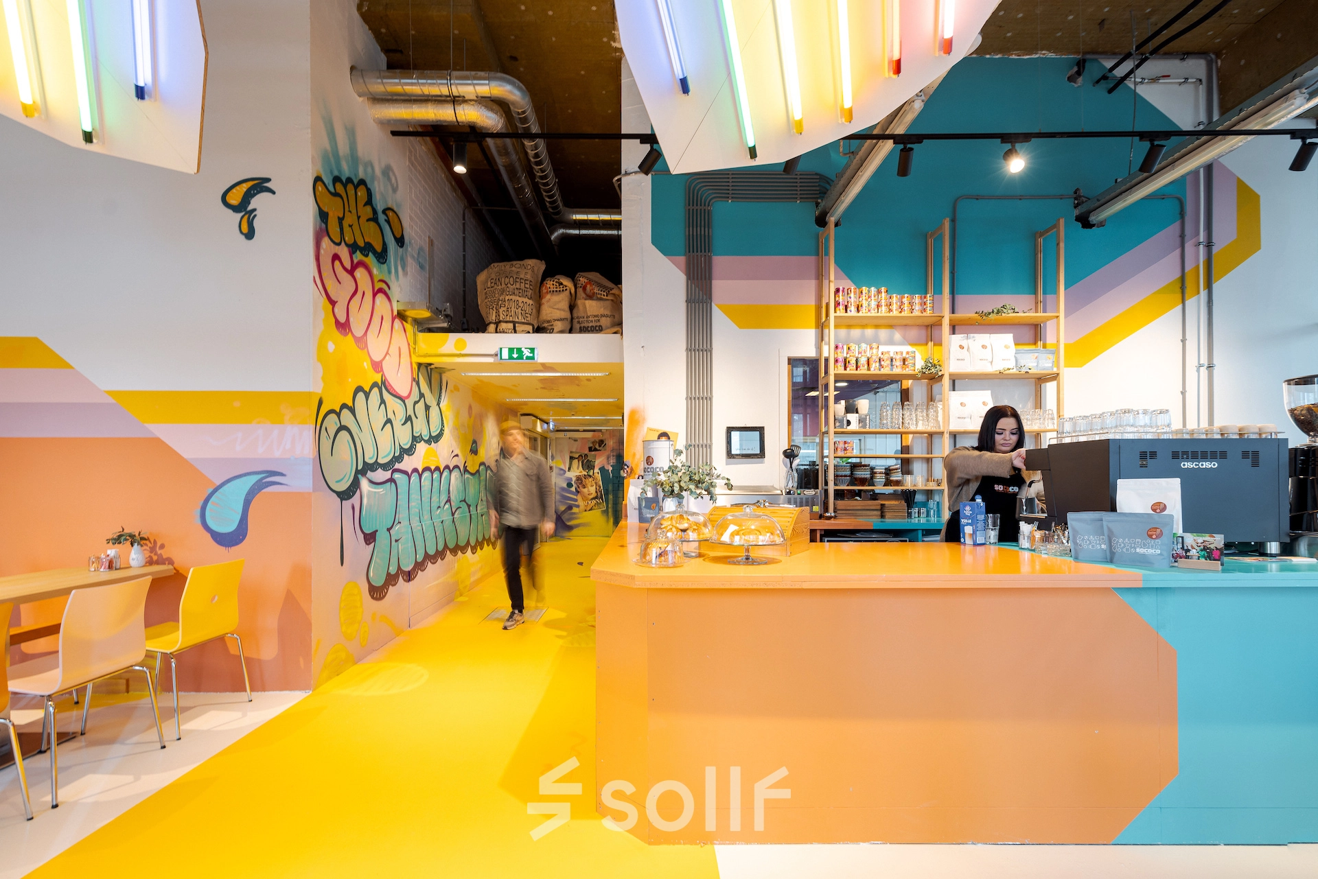 Vibrant interior at Weena 70, Rotterdam Center, featuring colorful decor and a café area where a person is preparing a beverage, ideal for office space rental.