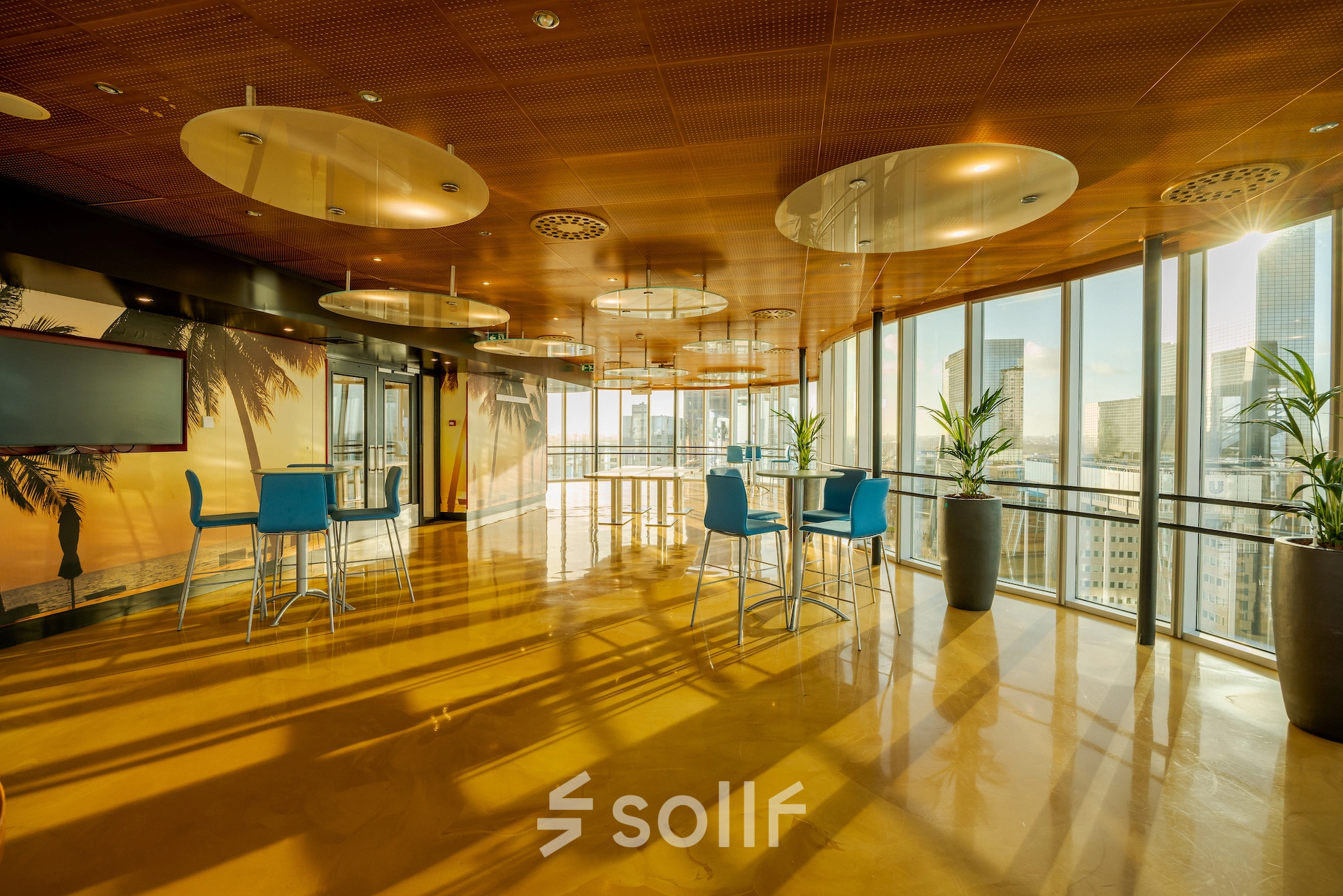 Bright office space rental at Weena 70, Rotterdam Center, featuring tall windows, modern decor, and bar-height tables with blue chairs, overlooking cityscape.