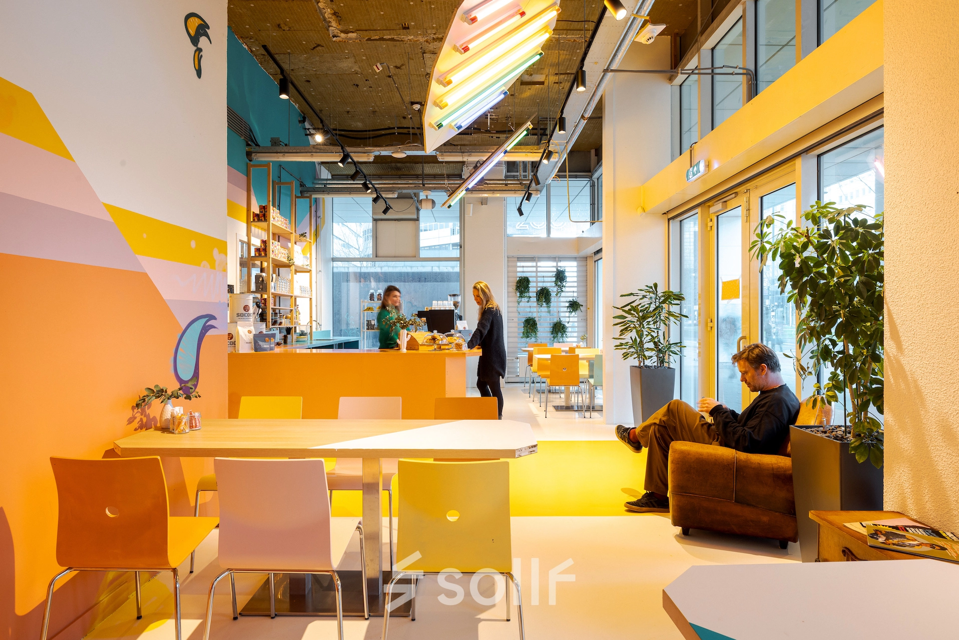 Lively office space at Weena 70, Rotterdam Center featuring a vibrant meeting and work area with people discussing and another person sitting. Ideal for office space rental.