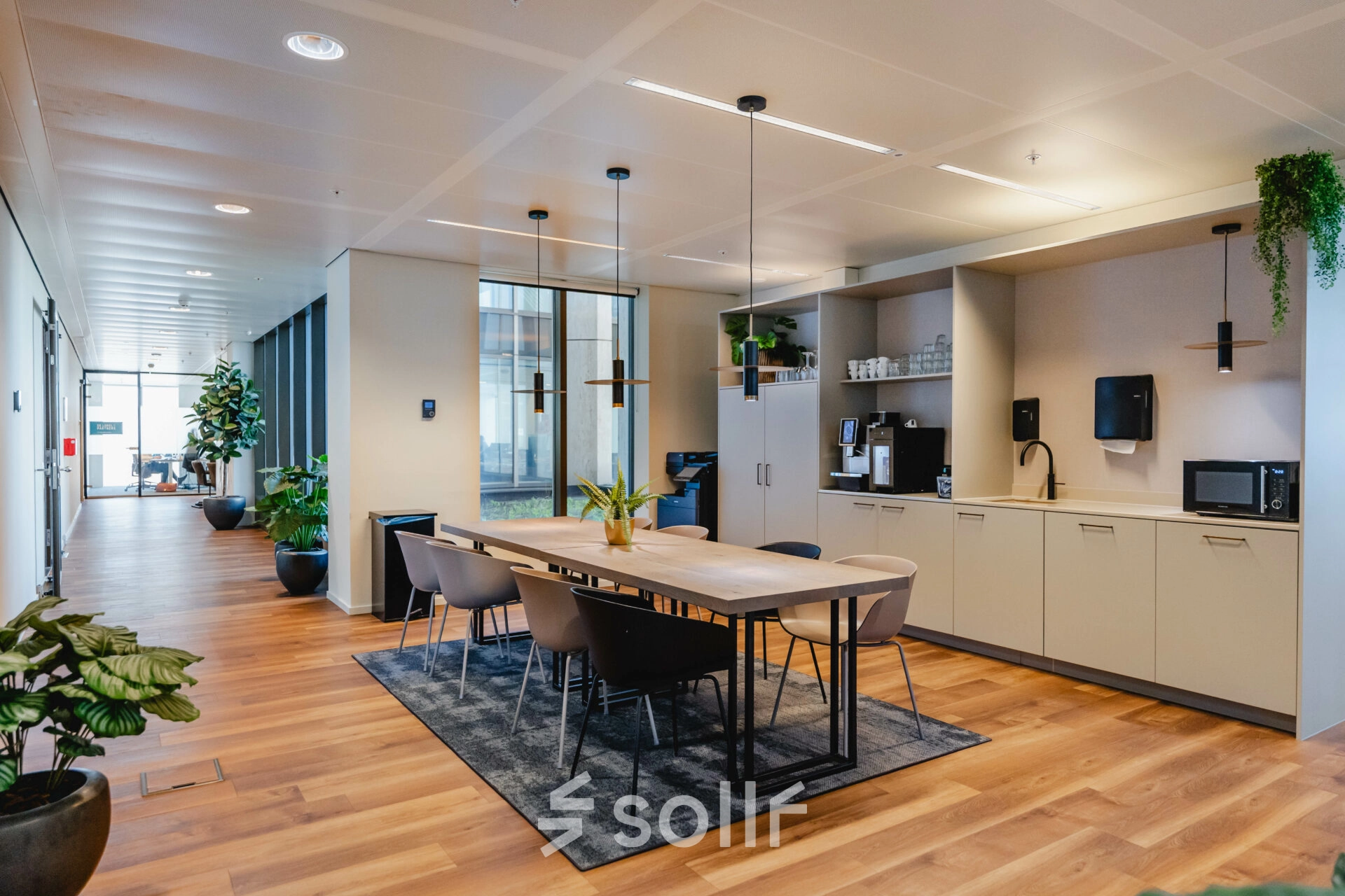 Modern office space at Weena 788, Rotterdam Center, featuring a furnished workspace with a long table, chairs, and kitchen facilities, ideal for office space rental.