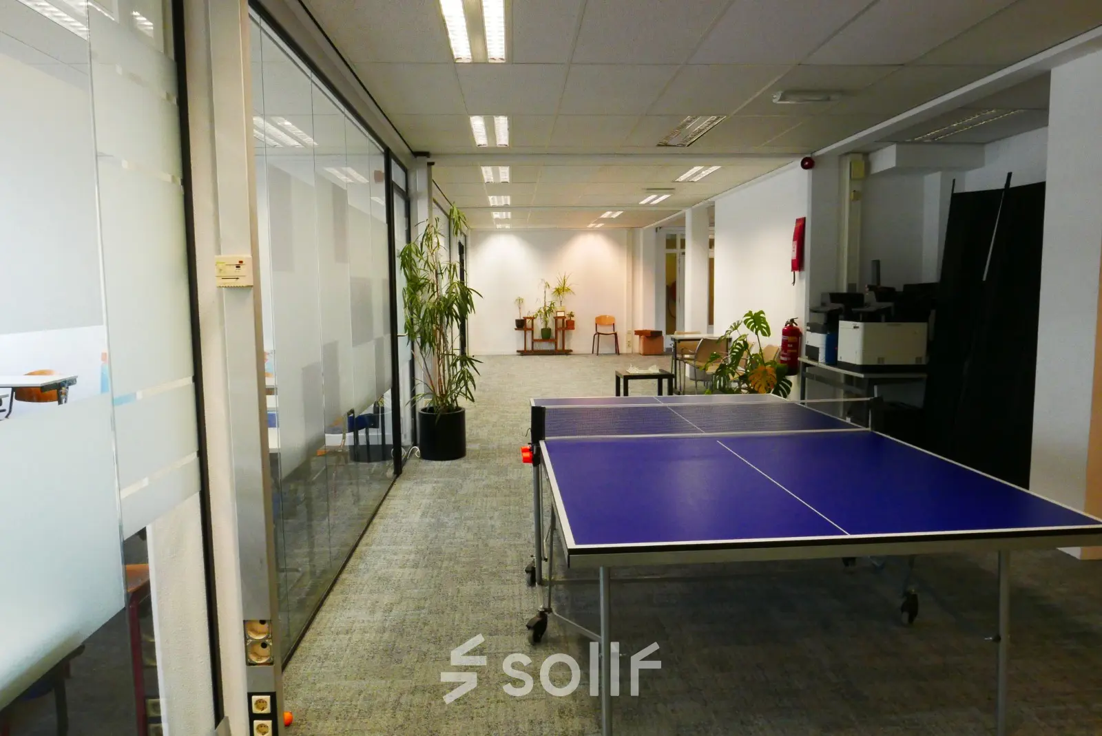 Spacious office at Wijnhaven 76, Rotterdam Center, featuring a casual meeting area with a ping pong table, plants, and seating. Ideal for office space rental.