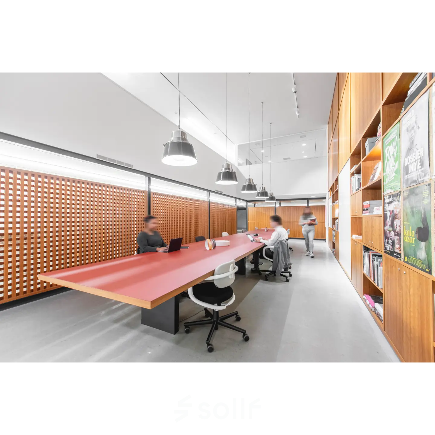 Modern office space at Hofplein 20, Rotterdam Central Station with a long shared desk, bookshelves, and people working on laptops. Ideal for office space rental.