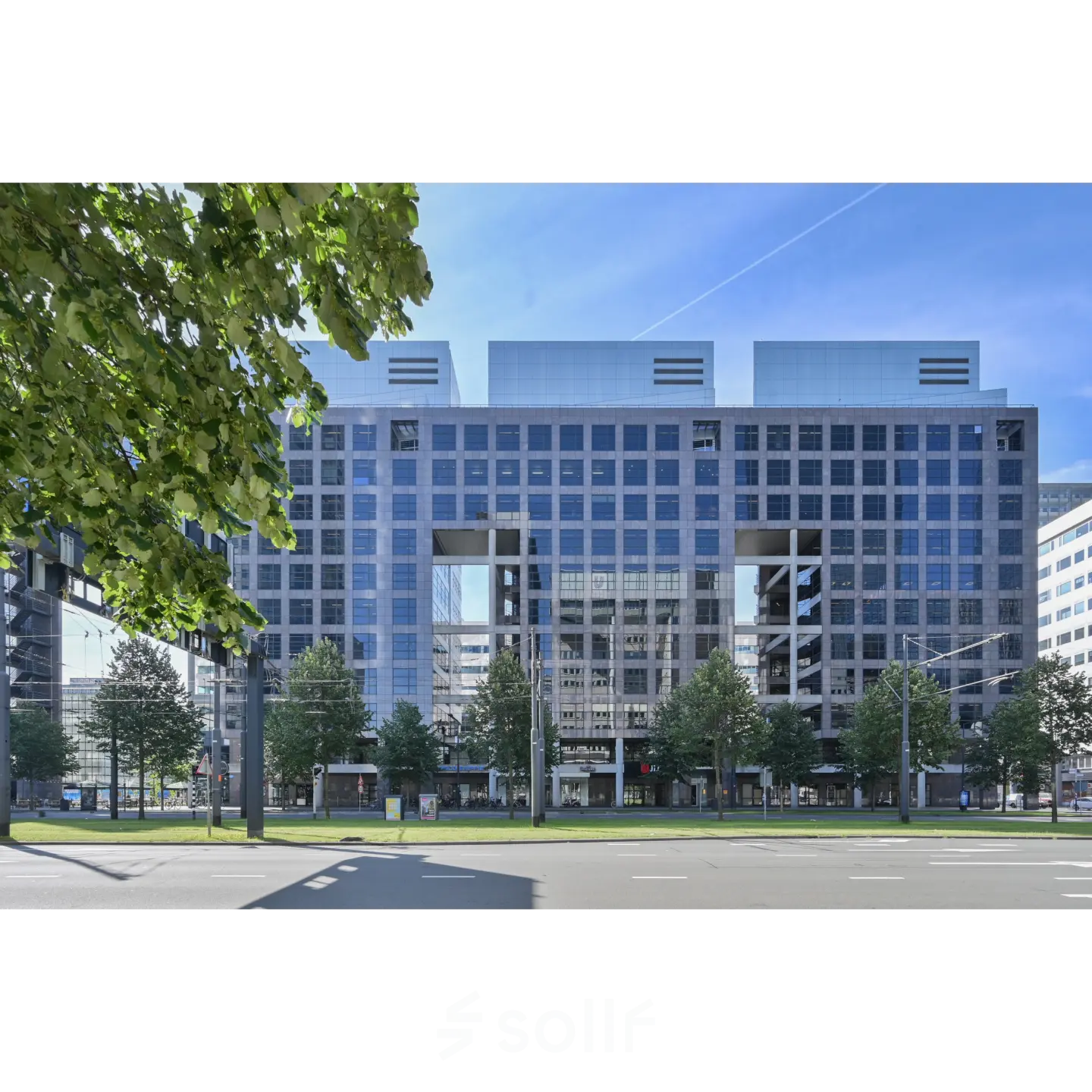 Exterior view of office space rental at Weena 290, Rotterdam Central Station, showcasing a modern building facade with large glass windows and surrounding greenery.