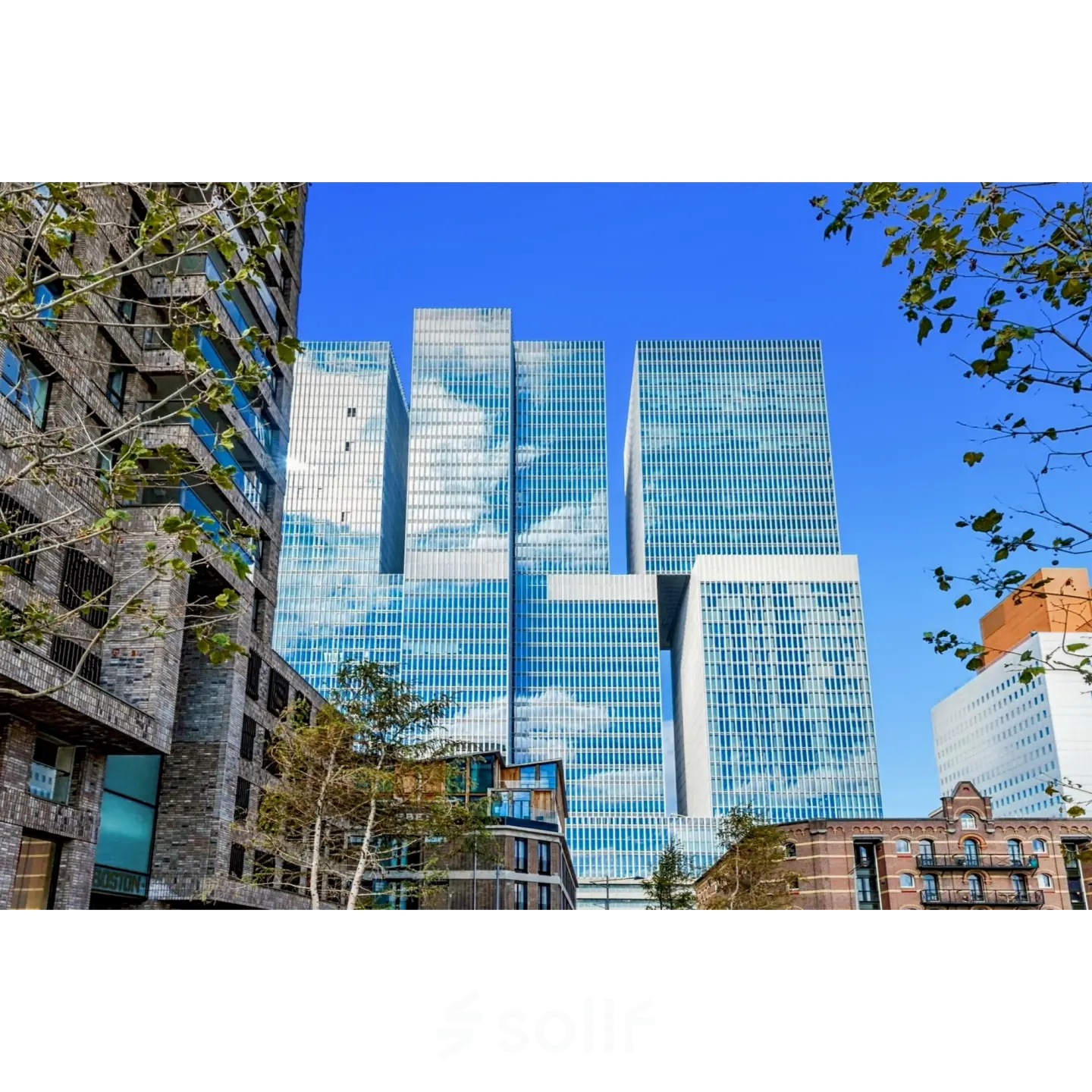 Exterior view of a modern office building located at Wilhelminakade 173, Rotterdam Kop van Zuid, ideal for office space rental with glass facade reflecting the blue sky.