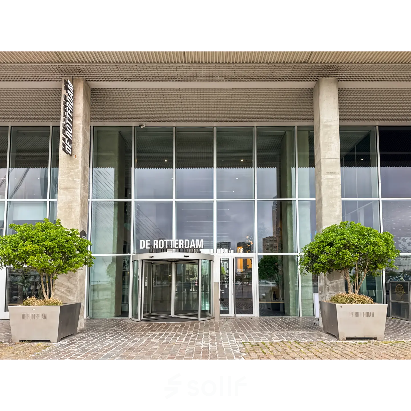 The modern entrance of an office building at Wilhelminakade 173, Rotterdam Kop van Zuid, showcasing a glass facade with large planters.