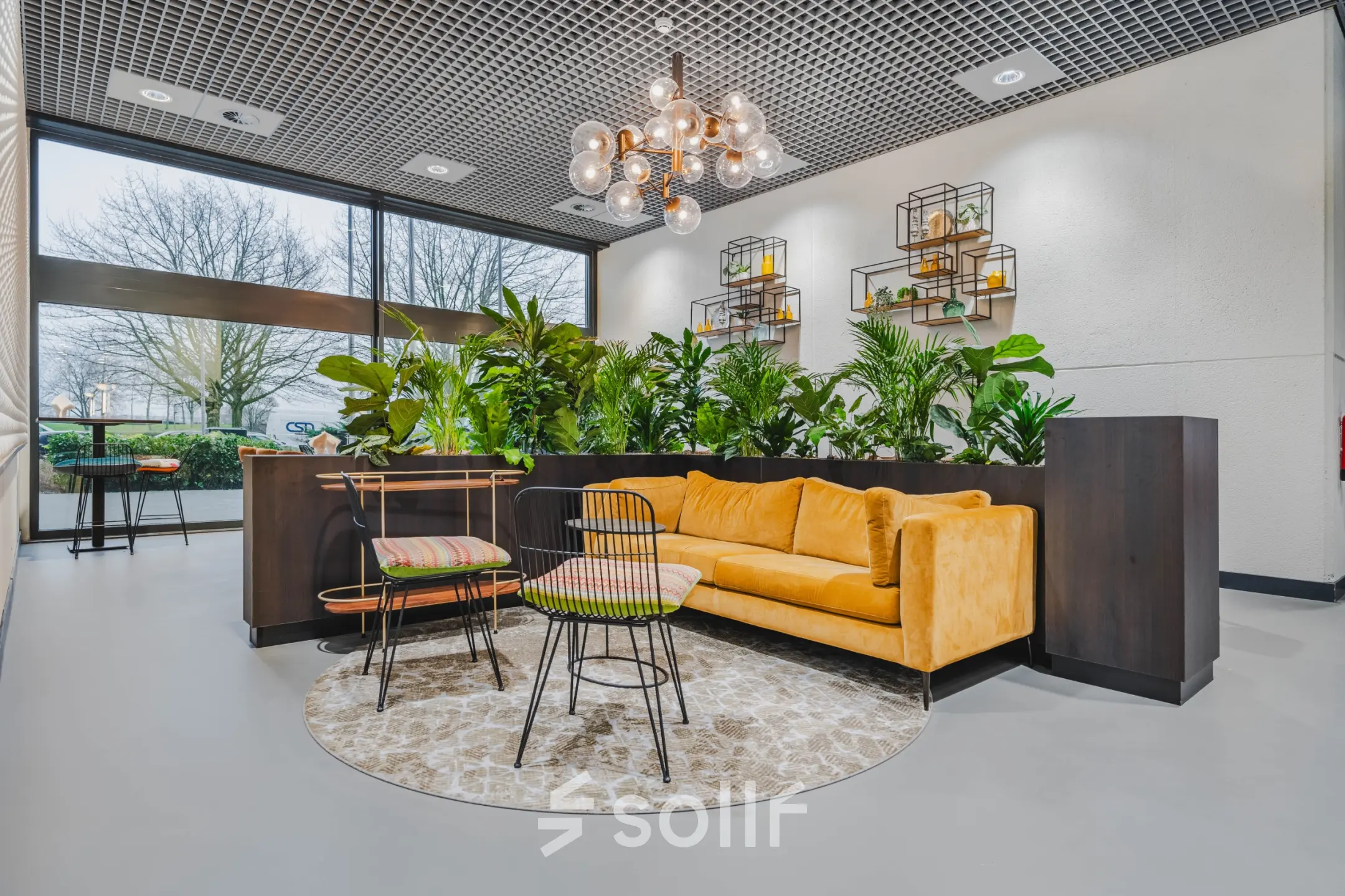 Modern lounge area with a mustard sofa, stylish chairs, and lush greenery at an office space rental in Rotterdam Kralingen.