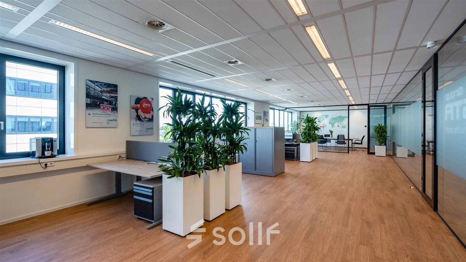 Spacious office space for rent in Rotterdam Waalhaven with modern decor, large windows, and plants. Features include desks and a meeting area.